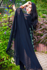 Naklejka premium Brunette woman in black sari and Indian adornment walks in summer park