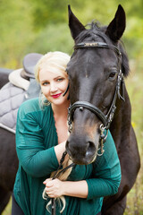 Blonde woman in green clothes and chestnut horse in park.