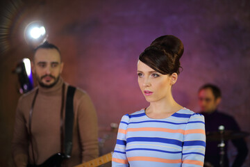 Portrait of beautiful singer with big eyes and dark hair in a striped dress in front of a drummer...