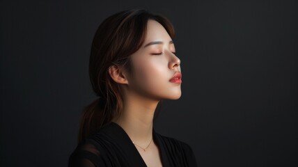 portrait of korean young woman with eyes closed on dark background
