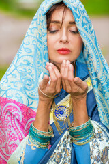 Middle age woman in blue sari and Indian adornment poses in garden