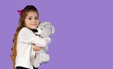 In the photo, it is captured how a little girl plays with her favorite toy, that is, a gray teddy bear, she is very happy and fascinated and holds it close to her chest so that she doesn't lose it.