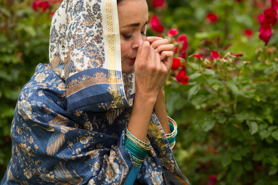 Woman in beautiful shawl and necklace prays among rose bushes in park