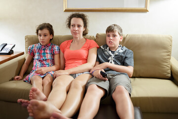 mother with two children watching tv on a coach