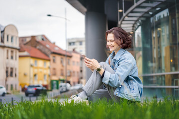 Young Caucasian woman using a smartphone while sitting near office building - 751668981