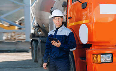 Dump truck driver man in uniform with tablet computer controls loading of cement to mixer on...