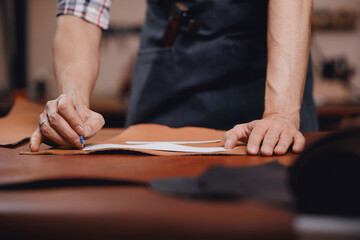 Closeup man tailor worker cobbler cuts out blanks for sewing bags or shoes according to pattern made of leather