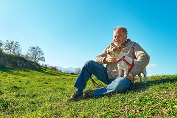 Naklejka na ściany i meble Gray haired man taking a walk with his jack russell dog in meadow in mountainous area. Mature man playing outdoors with his dog in nature.