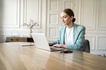 Focused professional woman working on laptop in a bright, elegant office, epitomizing modern...