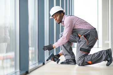 Fototapeta premium Construction african worker repairing plastic window with screwdriver indoors, space for text. Banner design