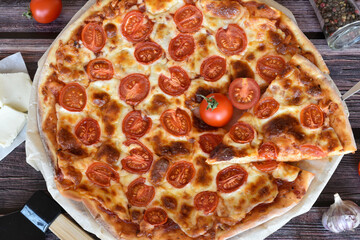 Shovel with slice of pizza. Fresh baked homemade pizza Margherita served on rustic wooden table. Red cherry tomatoes, mozzarella cheese, pizza cutter, pepper mill, garlic. Top view.