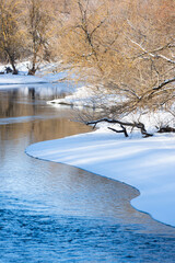 The river in winter, ripples on the water and snowy shores - 751682346