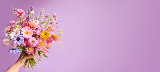Obraz na płótnie Canvas Colorful Mixed Bouquet Held in Hand Against Purple Background. Flower present. Summer garden bouquet. banner