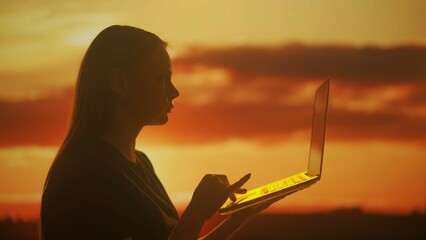 Silhouette of a woman working at a laptop at sunset