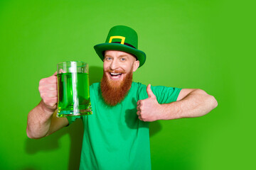 Photo of cheerful handsome guy hold beer cocktail mug show thumb up approve isolated on green color background