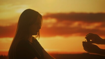 Silhouette of a woman looking at a box with an engagement ring at sunset