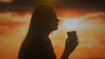 Silhouette of a woman drinking coffee at sunset