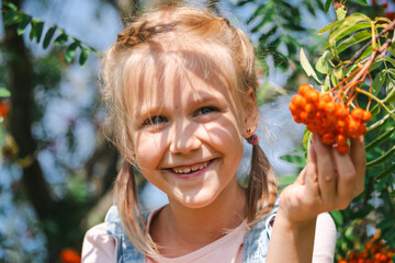 A radiant young girl beams with delight, clutching a cluster of orange berries in the glowing...