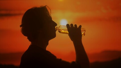 Silhouette of a Man Drinking Water Against a Sunset Background