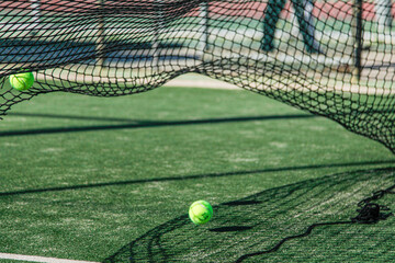 Two tennis or padel  balls on a vibrant green court with a net casting intricate shadows, highlighting the dynamic and aesthetic elements of the sport.