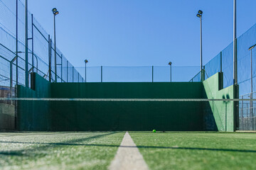 Empty paddle court, green walls, blue sky, and a resting ball