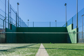 Fototapeta na wymiar Empty paddle court, green walls, blue sky, and a resting ball