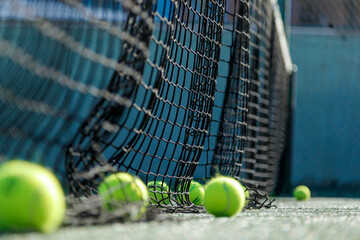 Tennis balls beside a net on a sunlit court