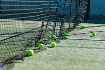 Green tennis balls near a net on a sunlit court.