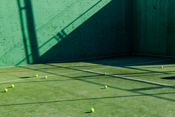 Tennis balls on green court with elongated shadows.