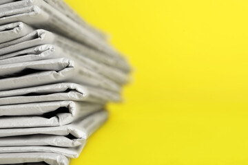 Stack of newspapers on yellow background, closeup with space for text. Journalist's work