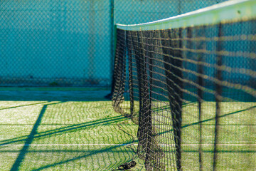 Empty tennis court, net and shadows at sunset.