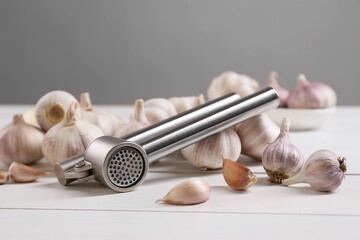 Metal press and garlic on white table, closeup