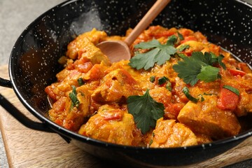 Delicious chicken curry in frying pan and spoon on table, closeup