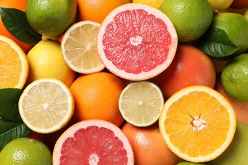 Different fresh citrus fruits and leaves as background, top view