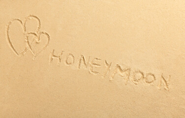 Word Honeymoon written on sand and hearts, top view