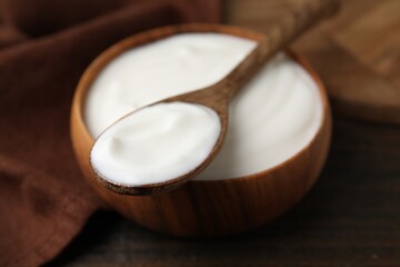 Delicious natural yogurt in bowl and spoon on wooden table, closeup