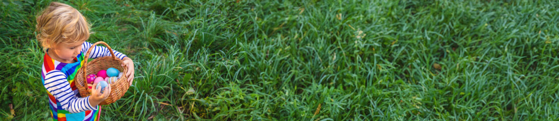 A child collects Easter eggs in the grass. Selective focus. - obrazy, fototapety, plakaty
