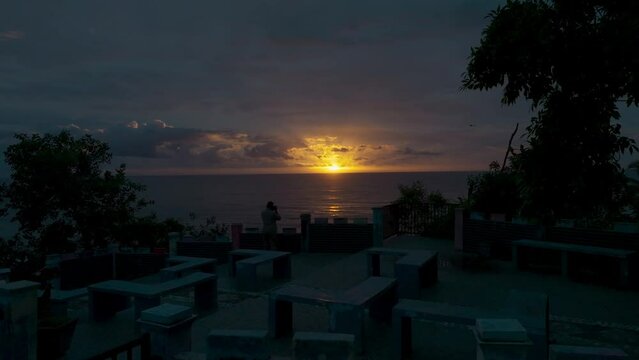 A man photographs the sunset from the edge of a coastal cliff