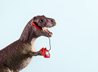 Cute dinosaur speaking on retro phone on blue background. Copy space.