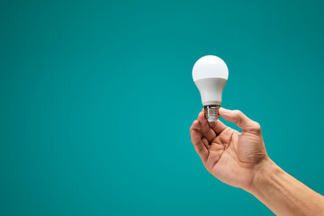 Hand holding a LED light bulb isolation on green background. Male hand demonstrating Eco power light bulb. Innovation inspiration concept.