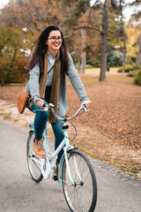 Cheerful young female prentice riding a bicycle in city park while rushing to work in her new company. Happy woman enjoying outdoors.