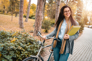 Beautiful female young adult taking a walk in public park. Smiling girl posing with her bike and...
