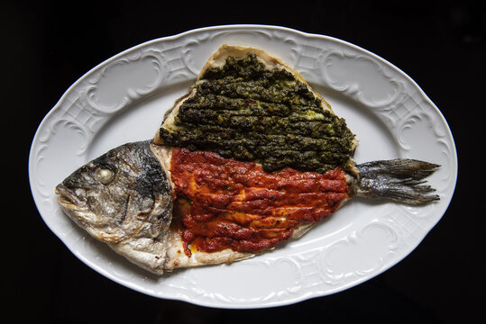 Whole fish on a plate in restaurant with red and green sauces
