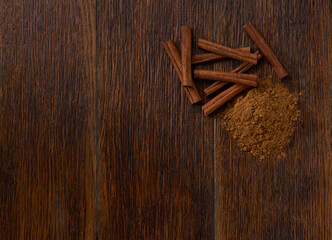 cinnamon sticks and cinnamon powder on a dark wooden table, top view.