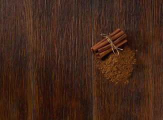 cinnamon sticks and cinnamon powder on a brown wooden table, top view.