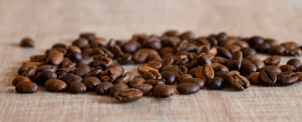 Coffee beans on a wooden table, selective focus, close-up, macro. Arabica or robusta coffee is scattered on the table, a banner.