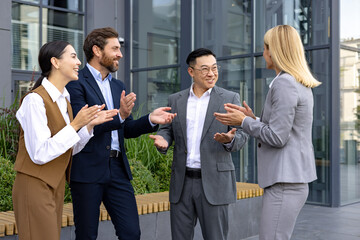 Group of happy business professionals clapping hands in celebration of a successful meeting outdoors near modern office.