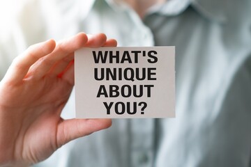 Close-up of a woman holding a card with the text Whats unique about you written on it.