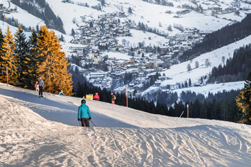 Skiers descend a snowy slope, with a picturesque snow-covered village nestled in the mountains...