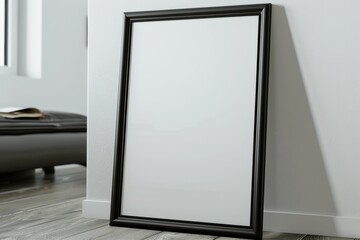 Empty thin black frame on light wooden floor with white wall behind it. Empty poster fram